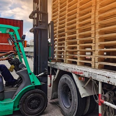 Forklift stacking wooden pallets on flatbed trailer